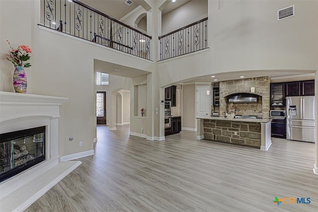 living area featuring visible vents, light wood finished floors, baseboards, arched walkways, and a glass covered fireplace