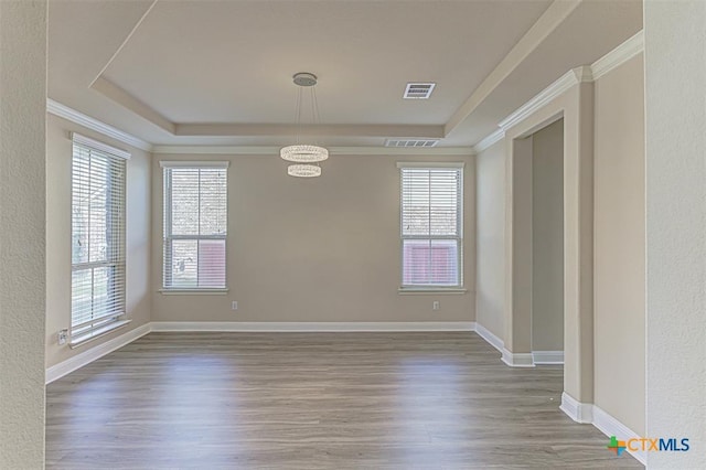 unfurnished room featuring a tray ceiling, wood finished floors, visible vents, and baseboards