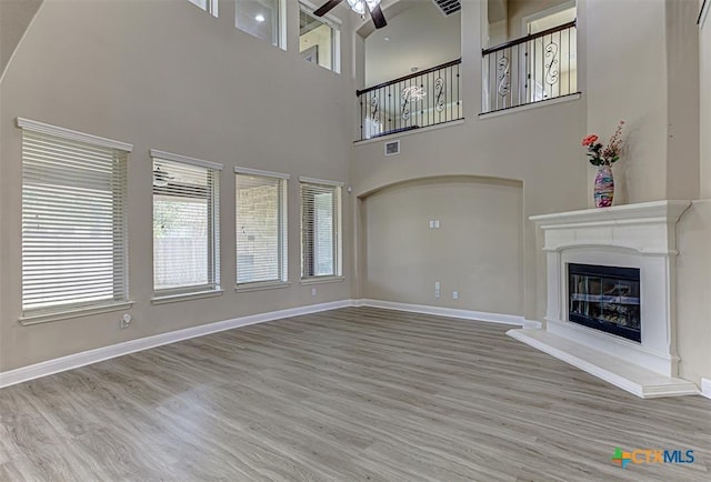 unfurnished living room with visible vents, a ceiling fan, a glass covered fireplace, wood finished floors, and baseboards