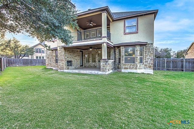 back of property with a ceiling fan, stone siding, a patio, a fenced backyard, and a balcony