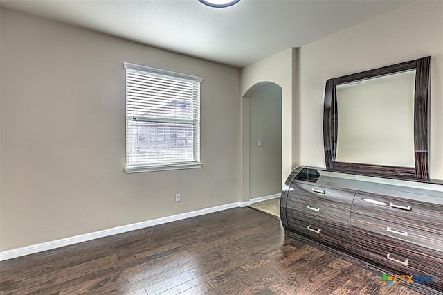 bedroom with arched walkways, baseboards, and dark wood-style flooring