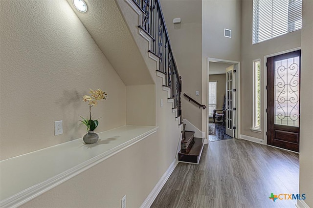 foyer with wood finished floors, visible vents, baseboards, stairs, and a towering ceiling