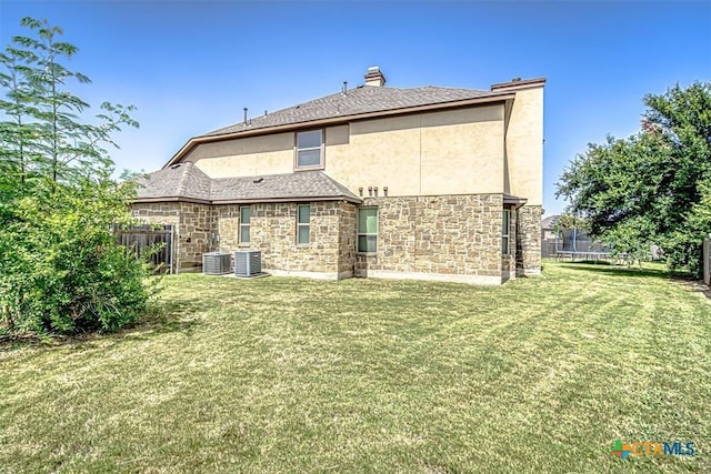 rear view of property featuring stone siding, a lawn, a trampoline, and fence