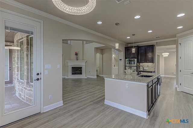 kitchen featuring a sink, light wood-type flooring, arched walkways, and ornamental molding