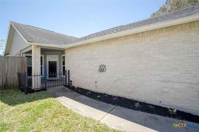 entrance to property with brick siding, roof with shingles, and fence