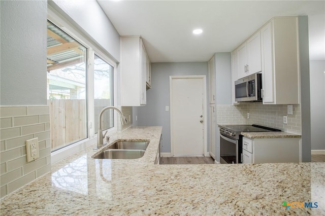 kitchen with light stone countertops, a sink, decorative backsplash, appliances with stainless steel finishes, and white cabinetry