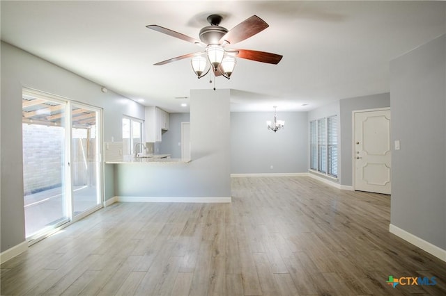 unfurnished living room with a sink, baseboards, ceiling fan with notable chandelier, and light wood finished floors