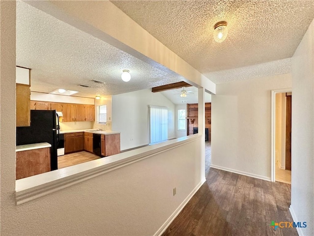 kitchen with light countertops, light wood-style floors, a brick fireplace, a sink, and black appliances