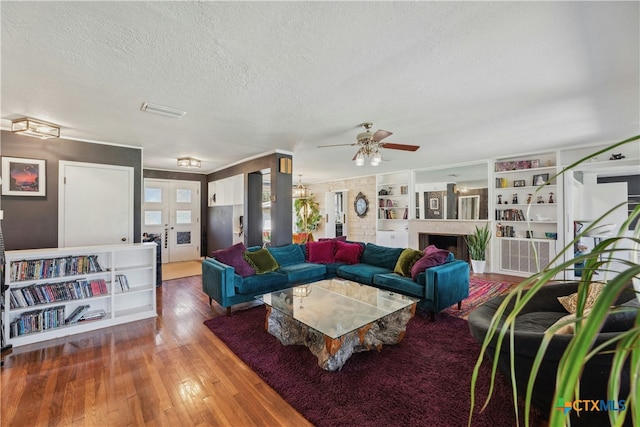 living room featuring a fireplace, visible vents, a ceiling fan, a textured ceiling, and hardwood / wood-style flooring