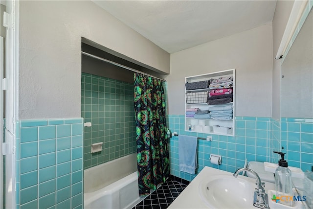 bathroom with a wainscoted wall, shower / tub combo, a sink, and tile walls