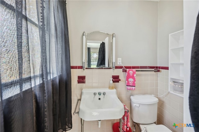 bathroom featuring wainscoting, a sink, toilet, and tile walls