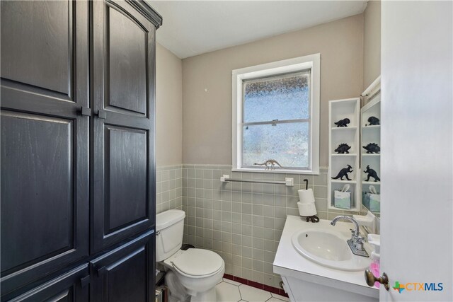 bathroom featuring toilet, a wainscoted wall, tile patterned floors, vanity, and tile walls