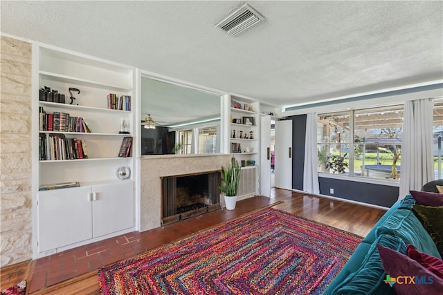 living room featuring built in features, visible vents, a fireplace, and a textured ceiling