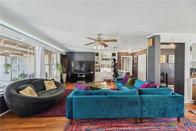 living room featuring wallpapered walls, visible vents, ceiling fan, wood finished floors, and built in shelves