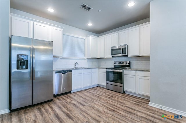 kitchen featuring hardwood / wood-style floors, sink, light stone counters, white cabinetry, and stainless steel appliances