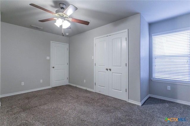 unfurnished bedroom featuring dark colored carpet, a closet, and ceiling fan