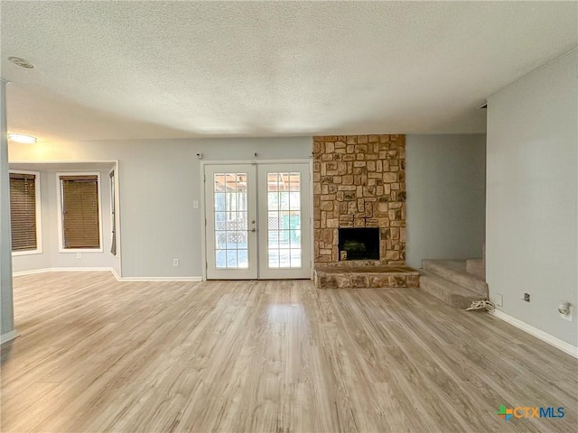 unfurnished living room featuring a textured ceiling, a fireplace, light hardwood / wood-style flooring, and french doors