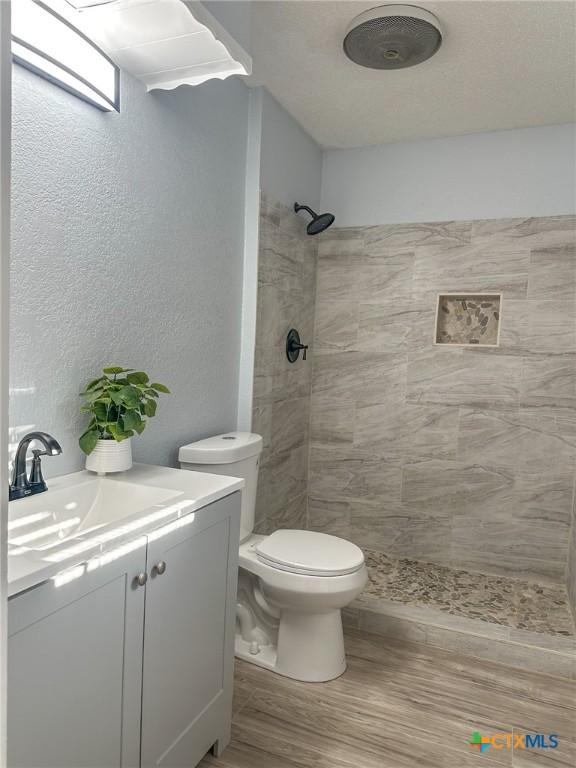 bathroom featuring tiled shower, vanity, hardwood / wood-style flooring, and toilet