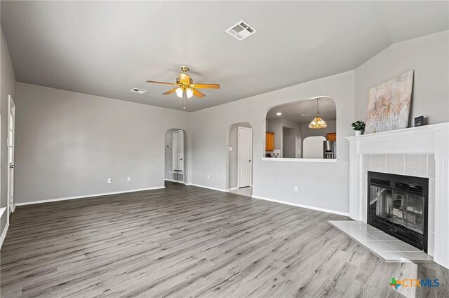 4504 Twin Oaks Cir, Killeen, TX 76542 - unfurnished living room featuring wood finished floors, ceiling fan, a tiled fireplace, and arched walkways