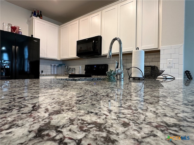 kitchen with white cabinets, black appliances, light stone counters, and backsplash