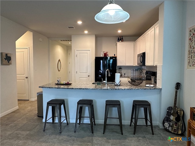 kitchen with dark stone counters, kitchen peninsula, black appliances, white cabinetry, and decorative light fixtures