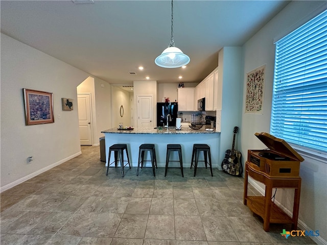 kitchen featuring white cabinetry, black fridge, kitchen peninsula, dark stone countertops, and pendant lighting