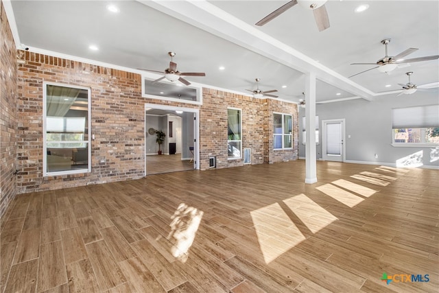 unfurnished living room featuring beam ceiling, light hardwood / wood-style floors, ornamental molding, and brick wall