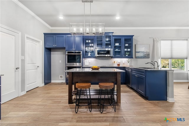 kitchen with pendant lighting, blue cabinets, stainless steel appliances, and a kitchen island with sink