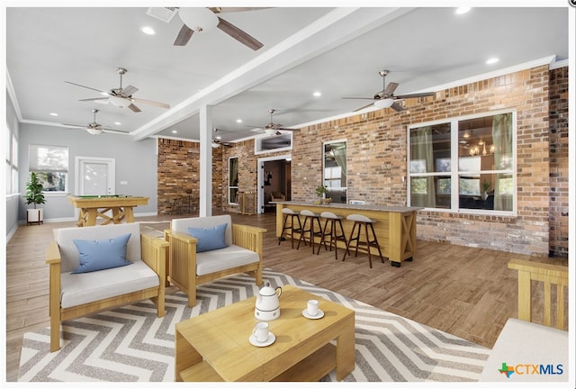 living room with beamed ceiling, light hardwood / wood-style floors, ornamental molding, and brick wall