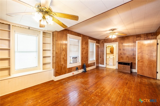 unfurnished living room featuring wood walls, ceiling fan, built in features, and dark hardwood / wood-style flooring