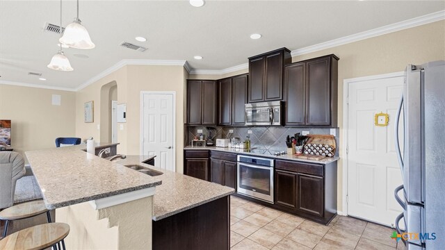 kitchen with stainless steel appliances, a center island with sink, sink, ornamental molding, and decorative light fixtures