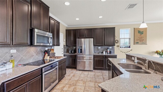 kitchen with light stone counters, appliances with stainless steel finishes, decorative light fixtures, dark brown cabinetry, and sink