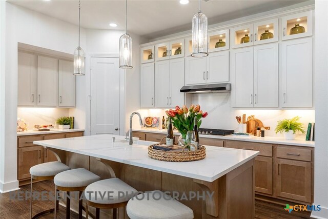 225 Dycus Bnd, Liberty Hill, TX 78642 - kitchen featuring under cabinet range hood, a breakfast bar area, light countertops, hanging light fixtures, and dark wood-type flooring