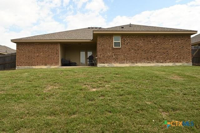 rear view of property featuring brick siding, fence, and a lawn