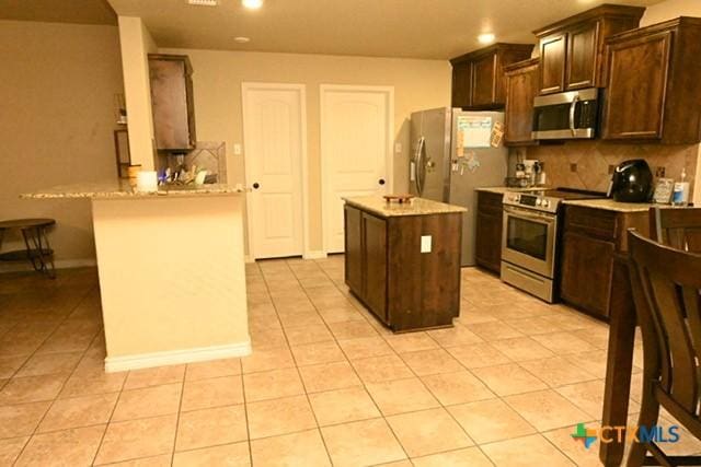 kitchen with light tile patterned floors, tasteful backsplash, appliances with stainless steel finishes, and a kitchen island