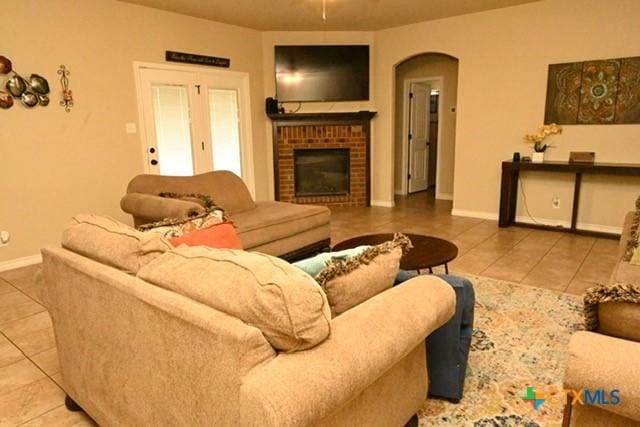 tiled living room featuring a brick fireplace, arched walkways, baseboards, and a ceiling fan