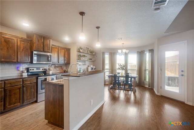 kitchen with a center island with sink, appliances with stainless steel finishes, hanging light fixtures, light hardwood / wood-style floors, and a chandelier