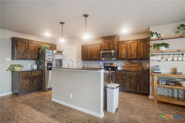 kitchen featuring stainless steel appliances, light wood-type flooring, a kitchen island with sink, pendant lighting, and decorative backsplash