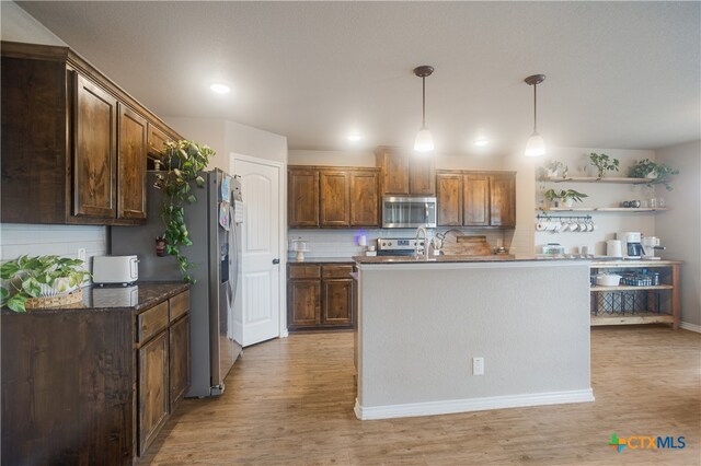 kitchen featuring light hardwood / wood-style floors, a center island with sink, appliances with stainless steel finishes, backsplash, and hanging light fixtures