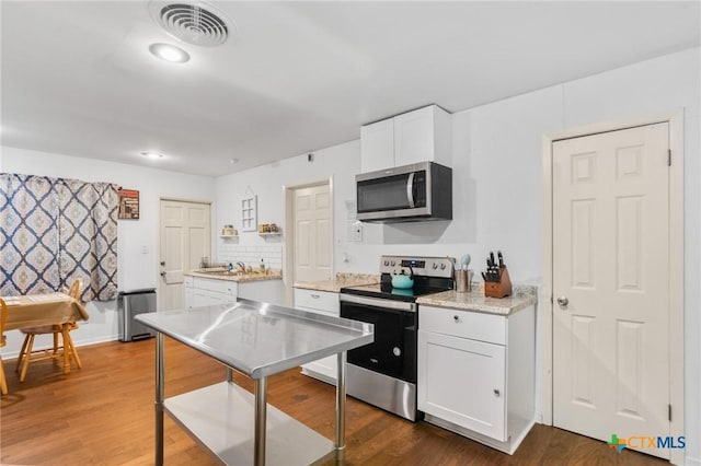 kitchen featuring visible vents, wood finished floors, a sink, stainless steel appliances, and white cabinetry