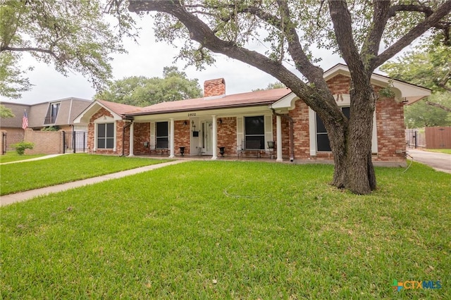 ranch-style house featuring a porch, a chimney, a front yard, brick siding, and fence