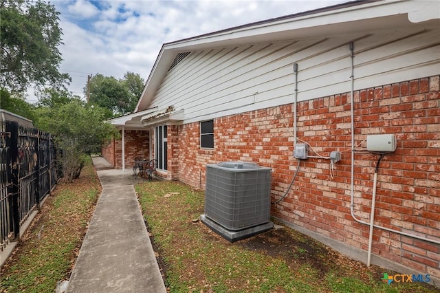 view of side of property with brick siding, fence, and cooling unit