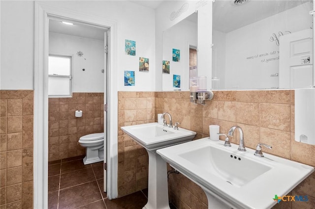 bathroom featuring tile patterned flooring, wainscoting, toilet, and tile walls
