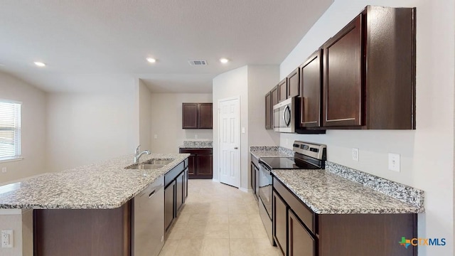 kitchen featuring sink, a kitchen island with sink, dark brown cabinets, stainless steel appliances, and light stone countertops