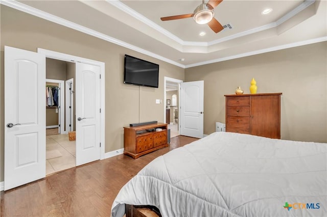 bedroom featuring ceiling fan, wood-type flooring, a tray ceiling, a closet, and ornamental molding