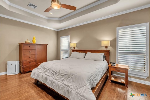 bedroom with hardwood / wood-style floors, ceiling fan, a raised ceiling, and ornamental molding