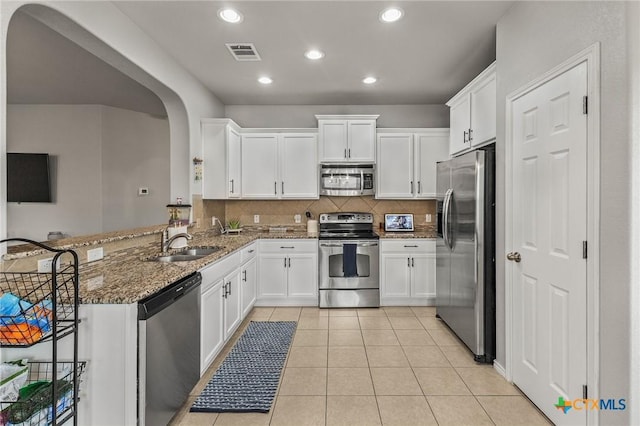 kitchen with visible vents, appliances with stainless steel finishes, arched walkways, a sink, and stone countertops