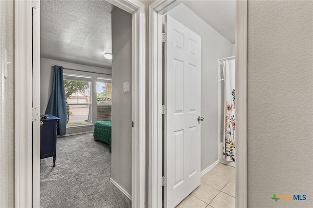 hallway with tile patterned floors, a textured wall, baseboards, and a textured ceiling