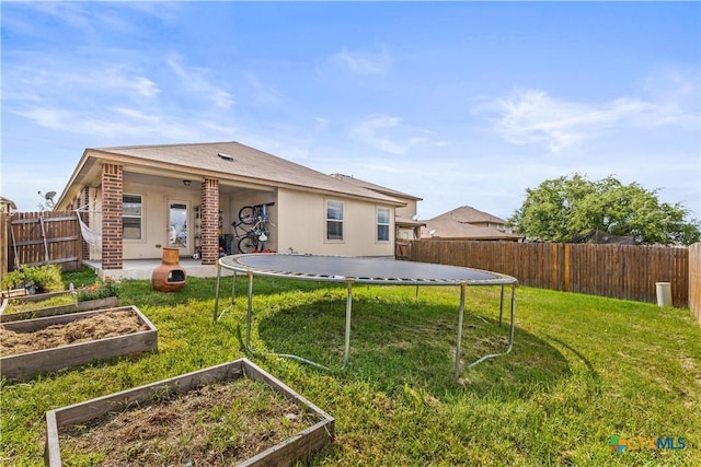 rear view of house with a lawn, a fenced backyard, a trampoline, and a vegetable garden