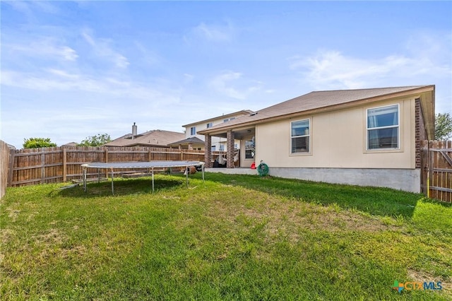 back of property with a fenced backyard, a trampoline, and a yard